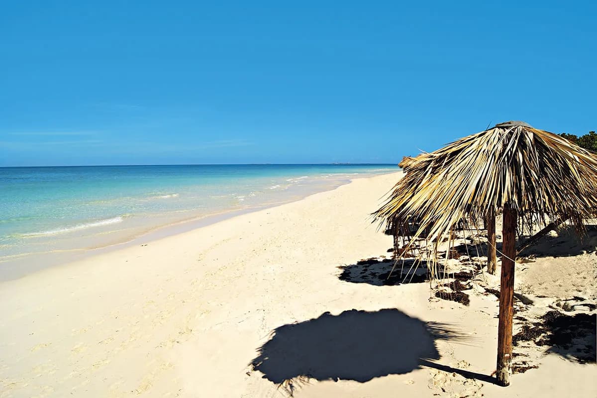 Pusta plaża z białym piaskiem przy hotelu Valentin Perla Blanca na Cayo Santa María, parasole z suchych liści palmowych i turkusowe, spokojne morze