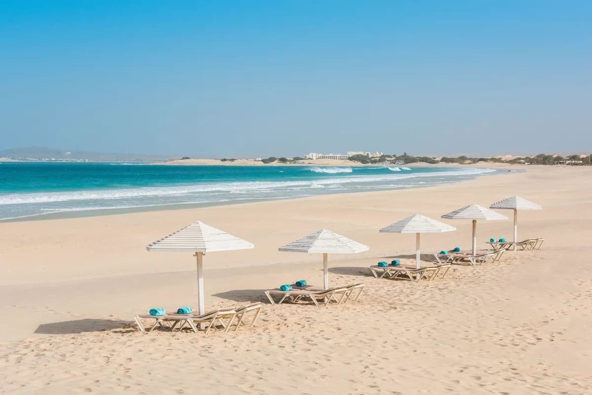 Szeroka plaża Praia de Chaves na Boa Vista z białymi parasolami i leżakami, turkusowym oceanem i wydmami na horyzoncie